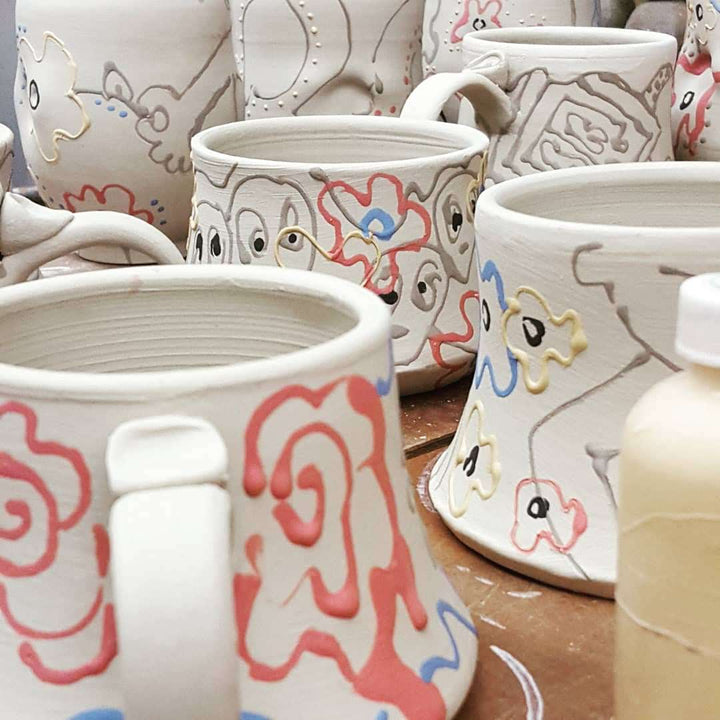 Collection of ceramic mugs with colorful designs on a wooden surface.