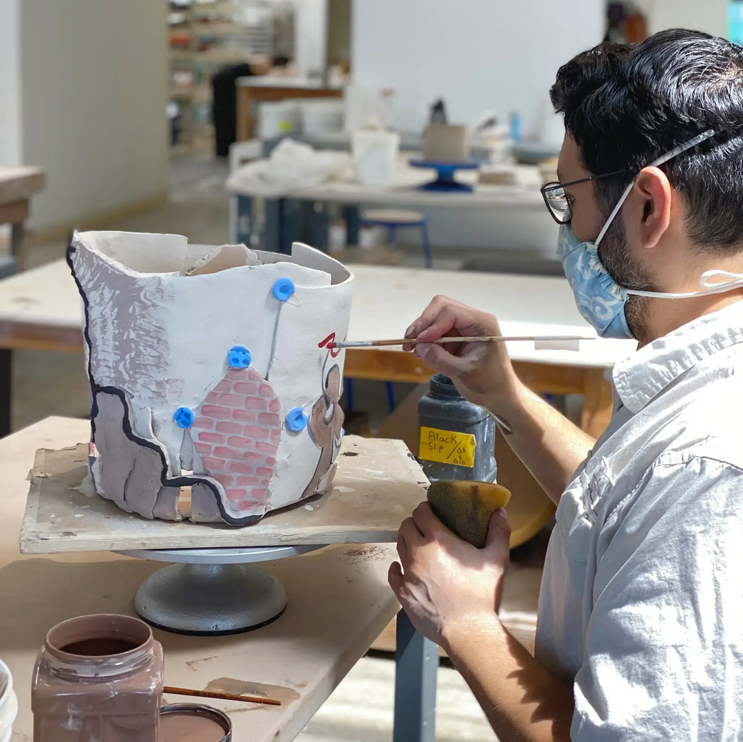 Person working on a ceramic piece with tools in a pottery studio.